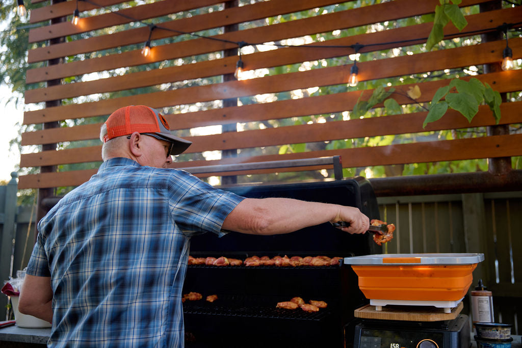 Man at grill moving wings into prep tub