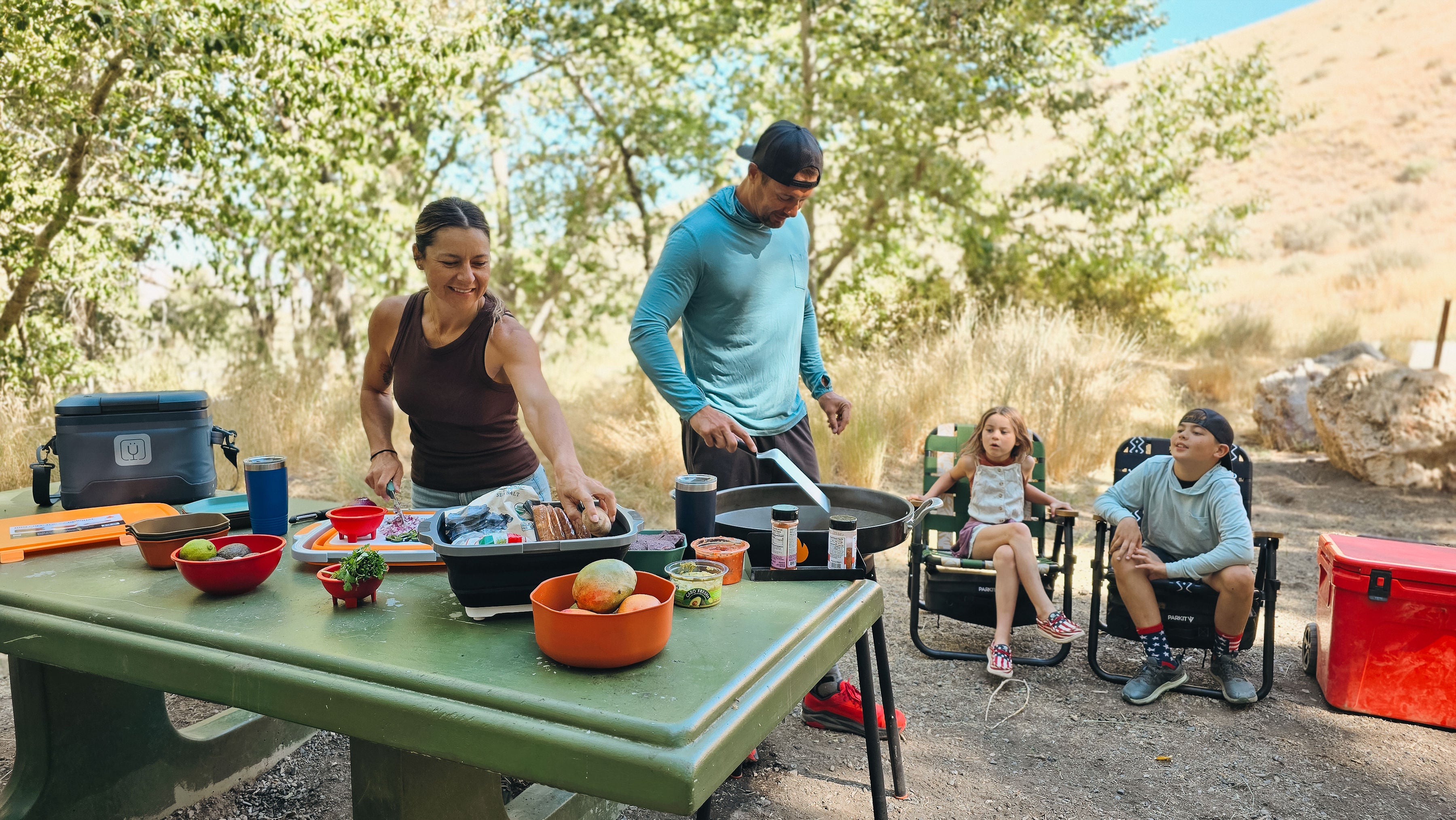 Family preparing food at a picnic table in a natural setting