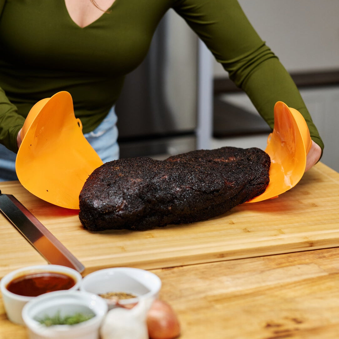 Woman preparing a large piece of meat on a wooden cutting board with various condiments.