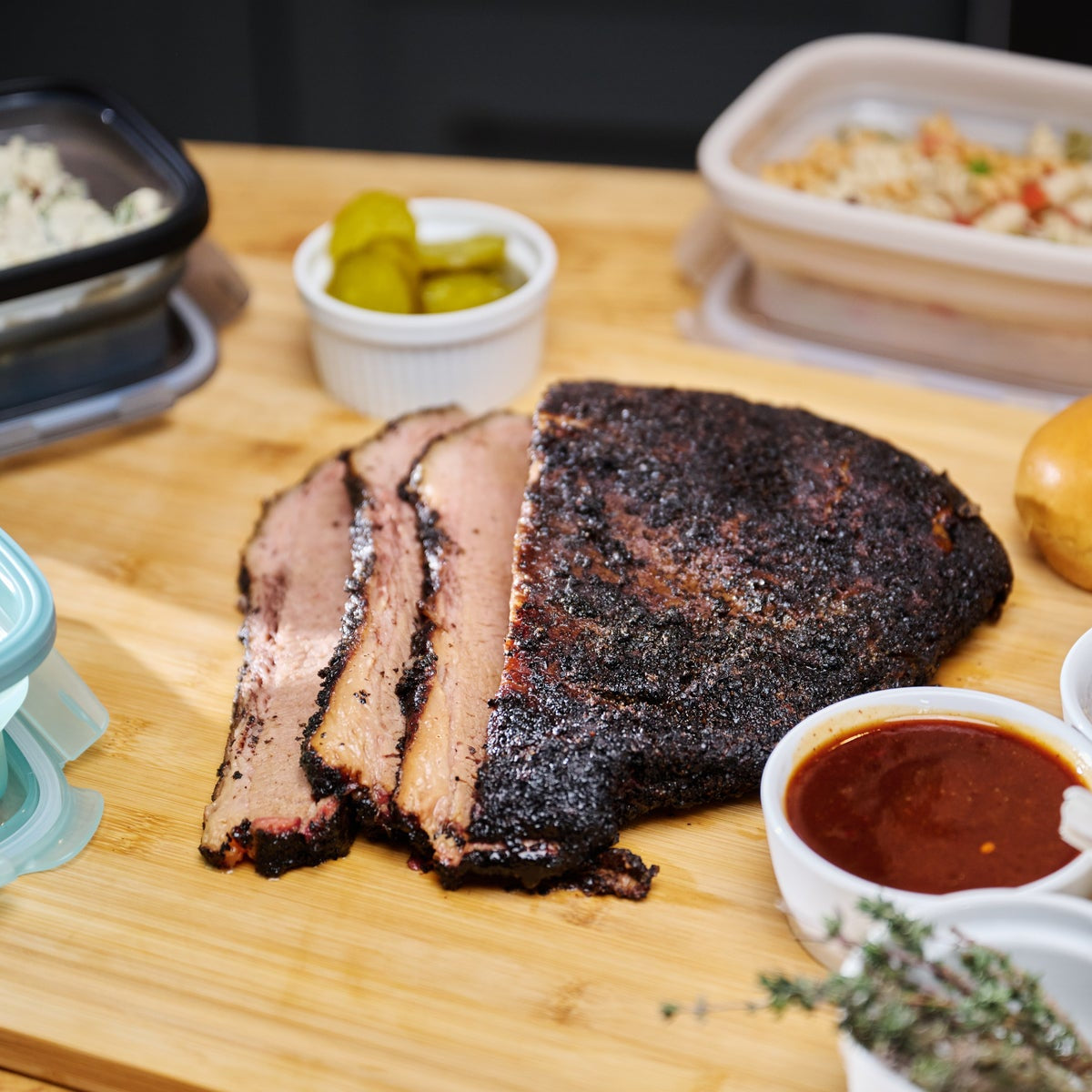Sliced brisket on a wooden cutting board with sides and condiments.
