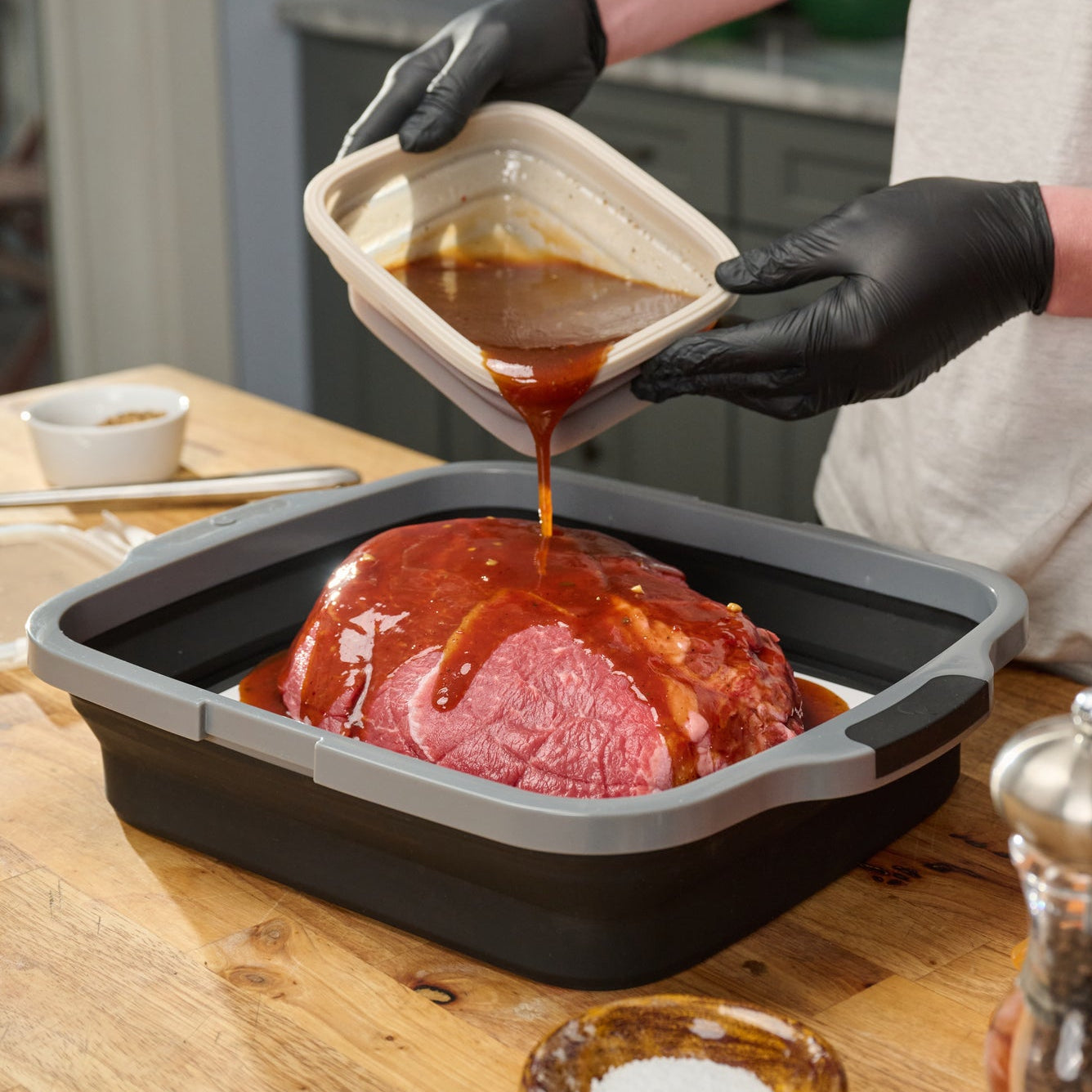 Person pouring sauce over a ham in a roasting pan in a kitchen.