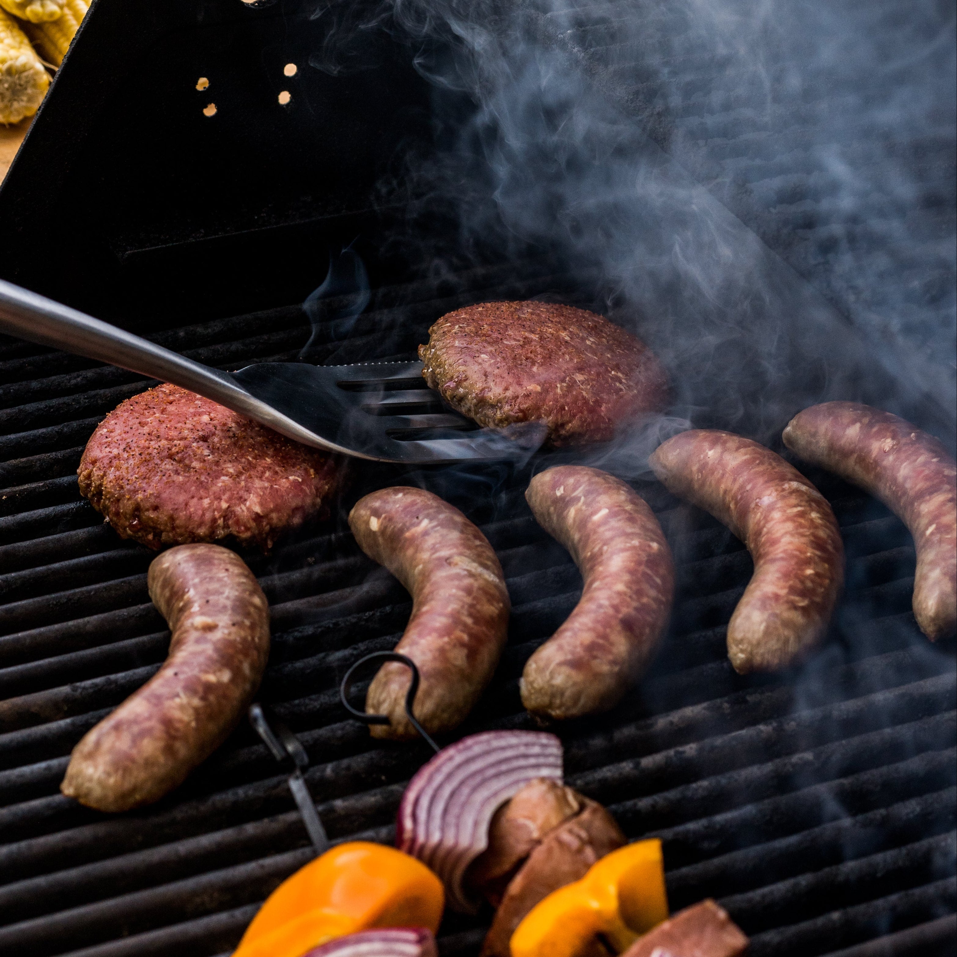 Grilling sausages, bell peppers, and onions with smoke rising from the grill.
